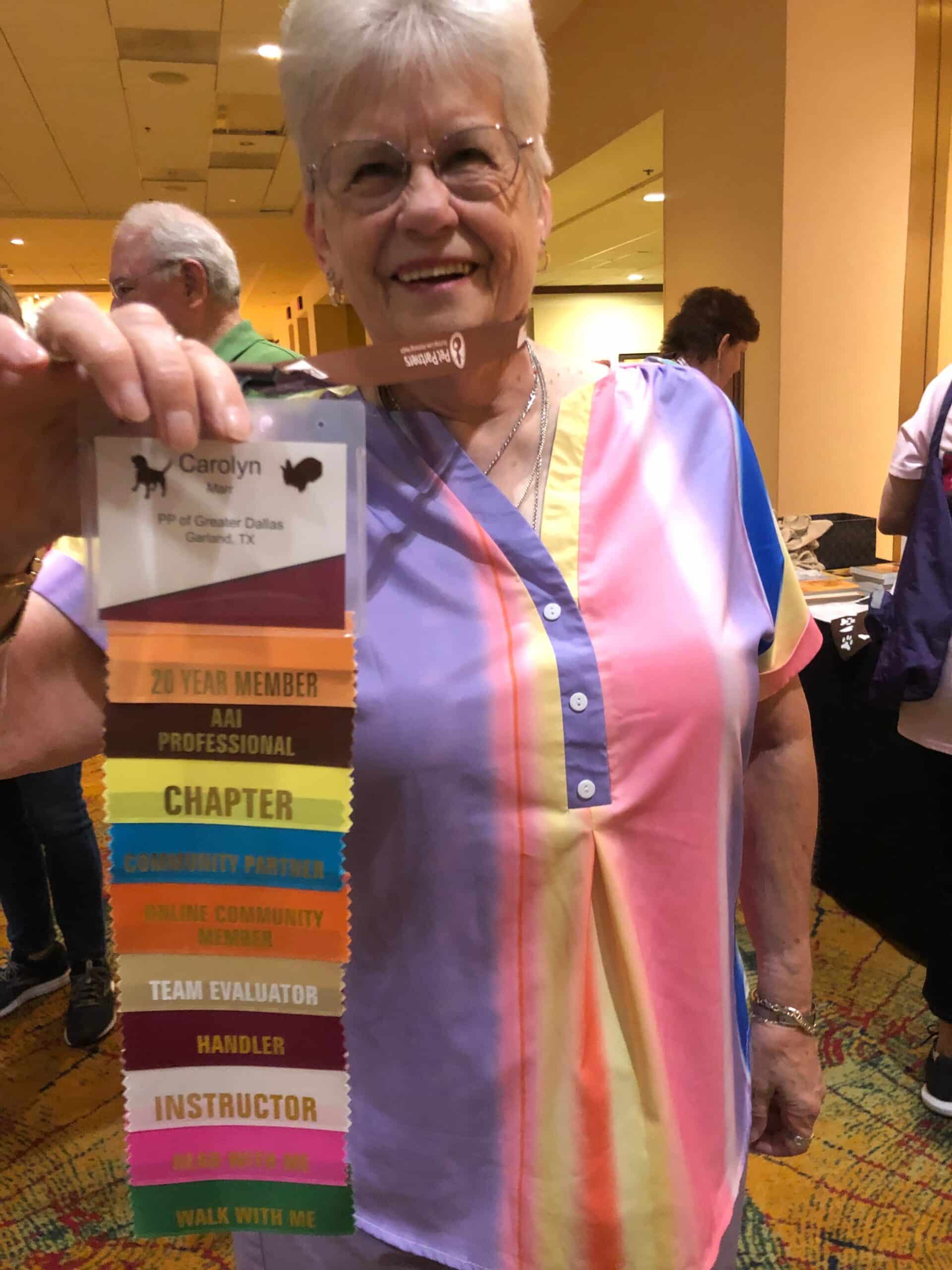 A smiling woman shows off a conference badge with a long string of identifying ribbons attached to it.