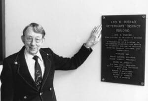 Dr. Leo Bustad points at a plaque on a wall.