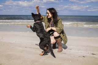 A woman playing with a brown and black dog on a beach