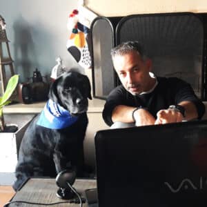 A black lab therapy dog and handler in front of a laptop for a virtual visit
