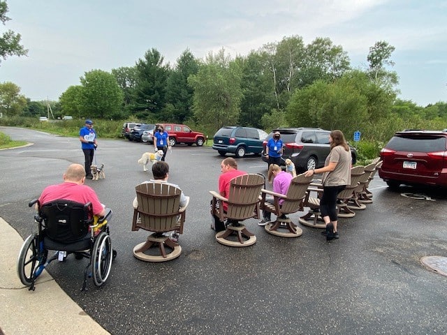 A group of residents at a care facility sitting outside and learning from therapy dog teams