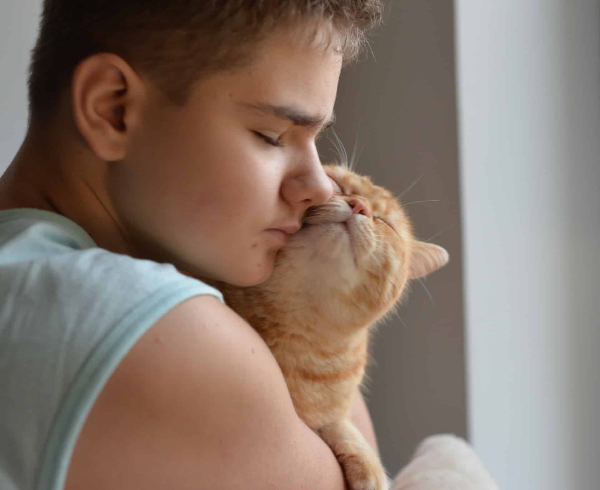A teen boy cuddles a happy orange tabby cat