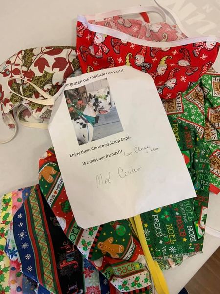 Christmas-themed surgical caps with a note that reads "We haven't forgotten our medical heroes! Enjoy these Christmas scrap caps. We miss our friends! Love, Chance & Marcia. There is also a picture of a great Dane therapy dog on the note.