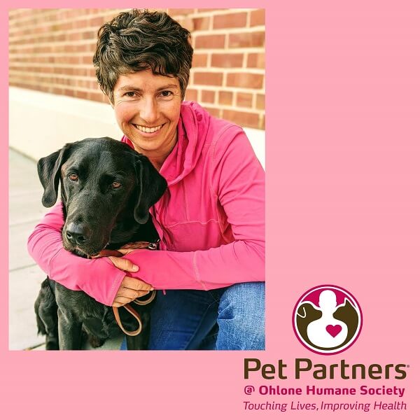 A woman cuddles a black Labrador retriever in a frame for Pet Partners @ Ohlone Humane Society