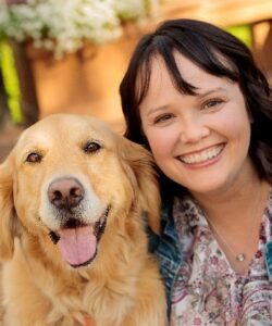 A happy golden retriever and a brown-haired woman smiling