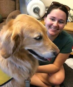 A smiling college student pets a golden retriever therapy dog