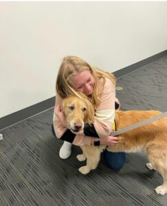 A visibly emotional college student hugs a golden retriever therapy dog.