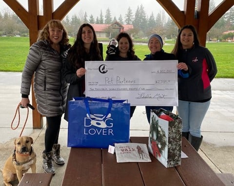 A group of people hold a ceremonial donation check from Dog Is Good for Good.