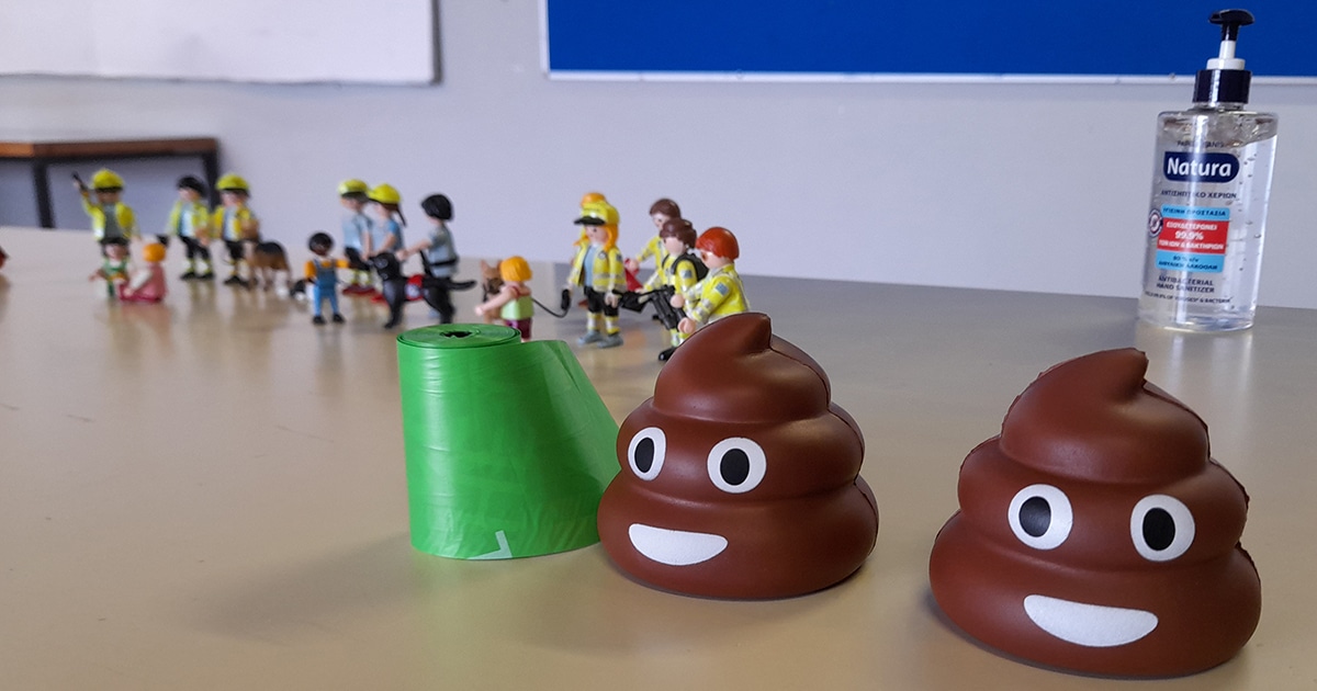A roll of pet waste bags, plush toys shaped like poop emoji, and a bottle of hand sanitize sit on a table.