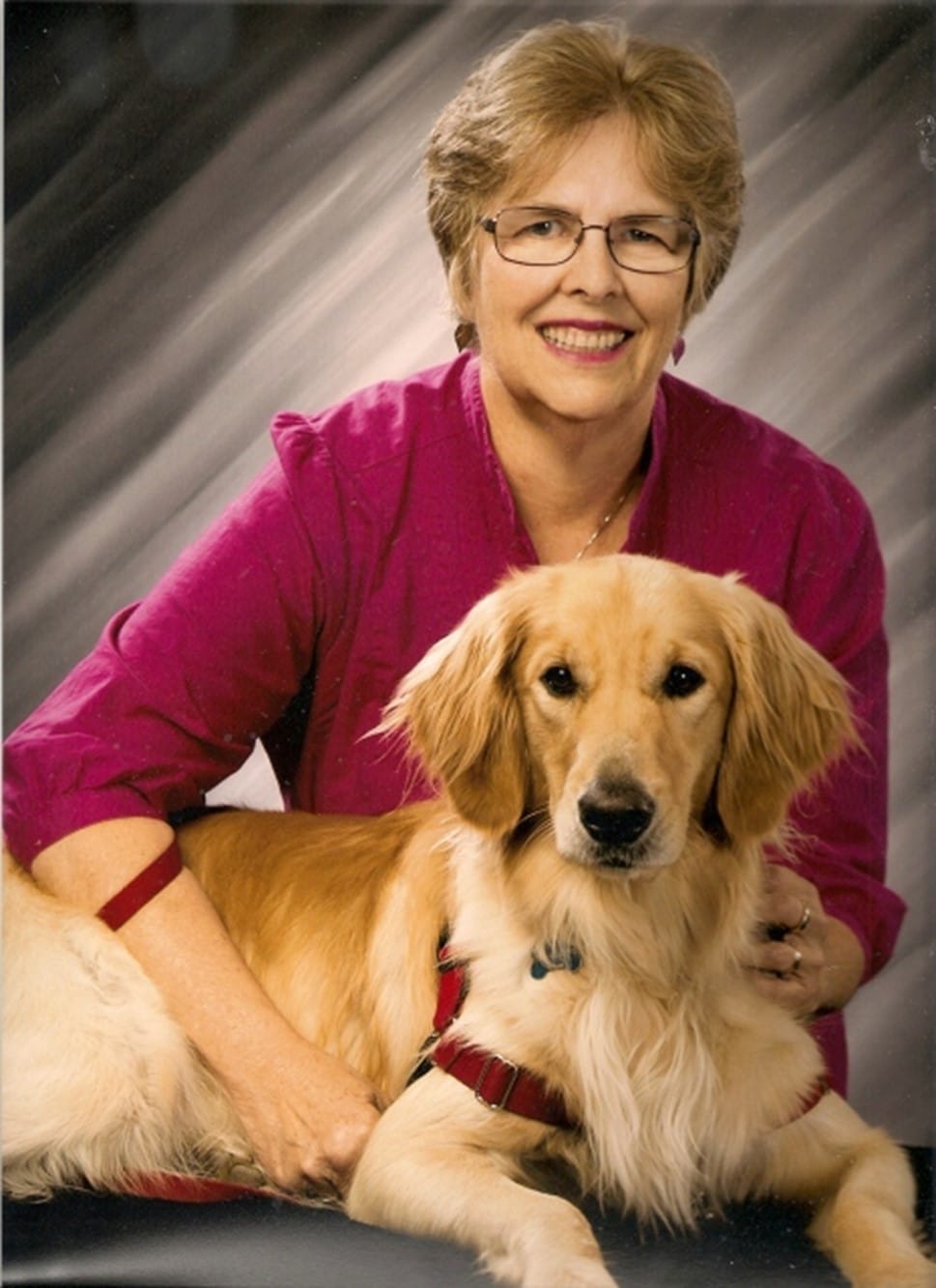 A smiling woman poses with her hands on a golden retriever.