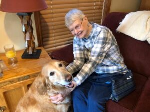 A smiling senior adult pets a golden retriever therapy dog, who has a happy expression.