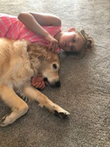 A child lies on her side on the floor, cuddler up to a golden retriever therapy dog who is asleep in the child's arms.