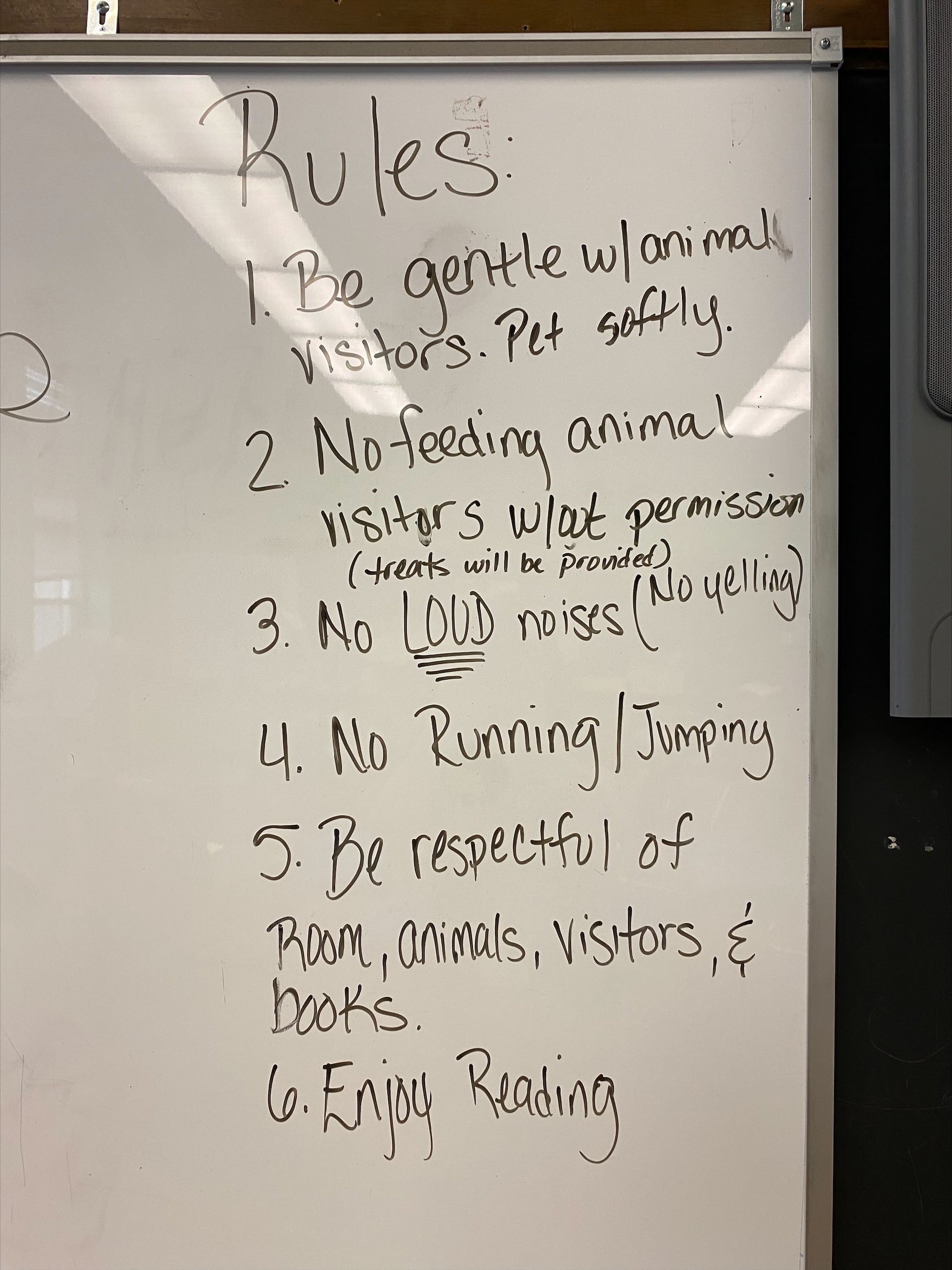 List of rules written on a white board for students who are visiting with a therapy dog for reading.