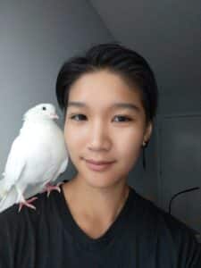 A person smiles for the camera with a white pigeon sitting on his shoulder