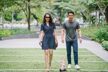 A woman and man walk a small mixed-breed dog in a park.