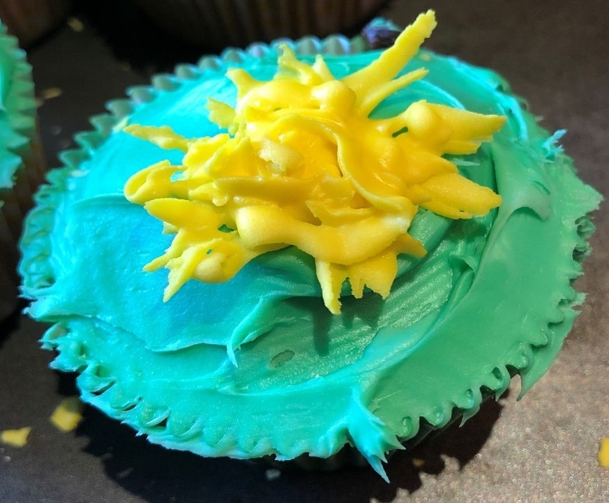 A cupcake with green frosting and a yellow frosting dandelion decoration.