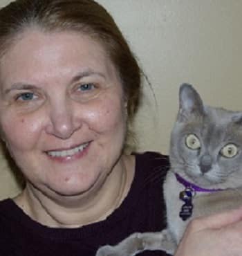 A smiling woman holds a Burmese therapy cat.