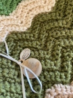 A dog name tag and a St. Jude medal pinned to a patterned blanket.