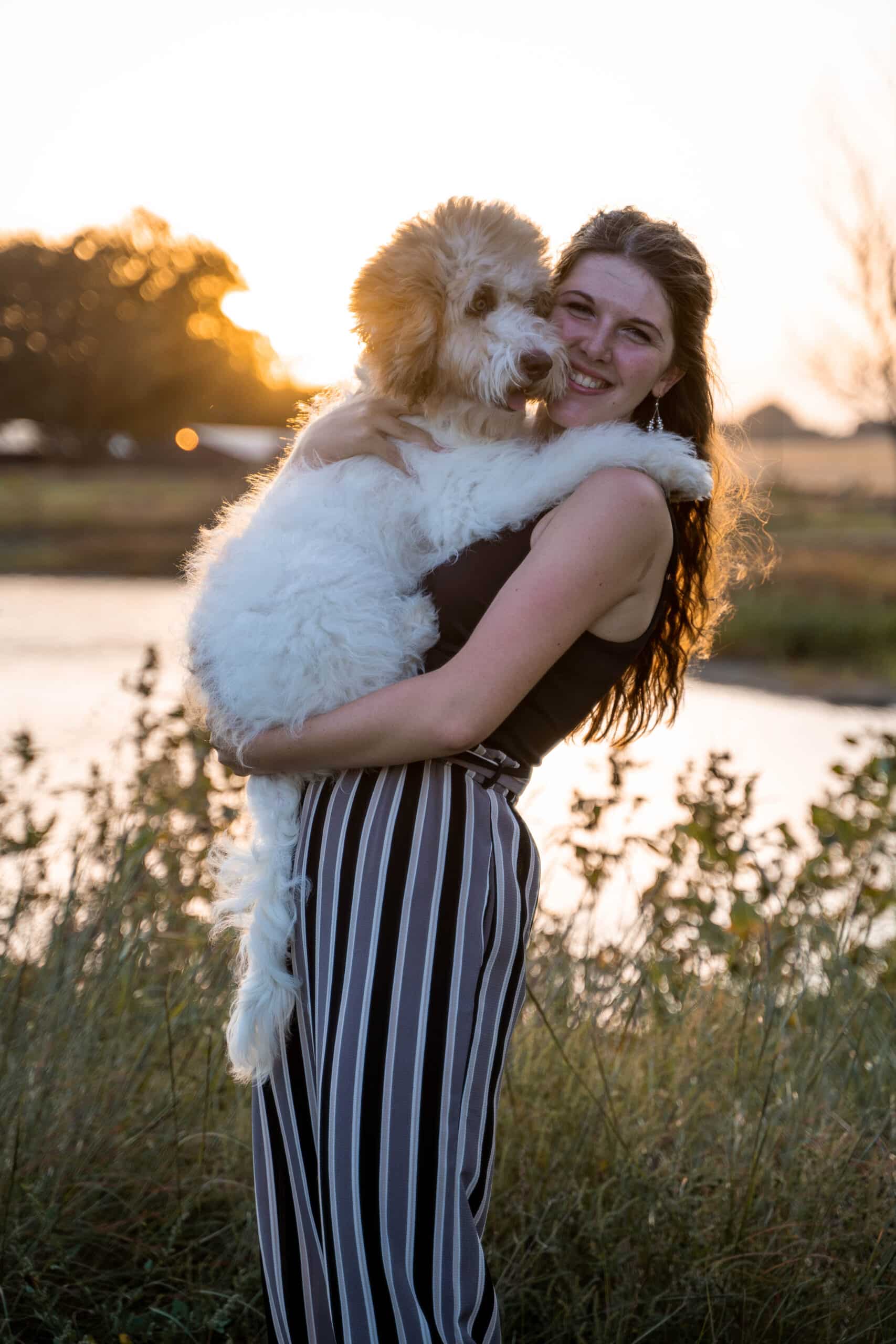 A ark-haired young woman, Kathryn Ribbens, poses in front of a lake holding a Bernedoodle dog. Photo provided by Kathryn Ribbens.