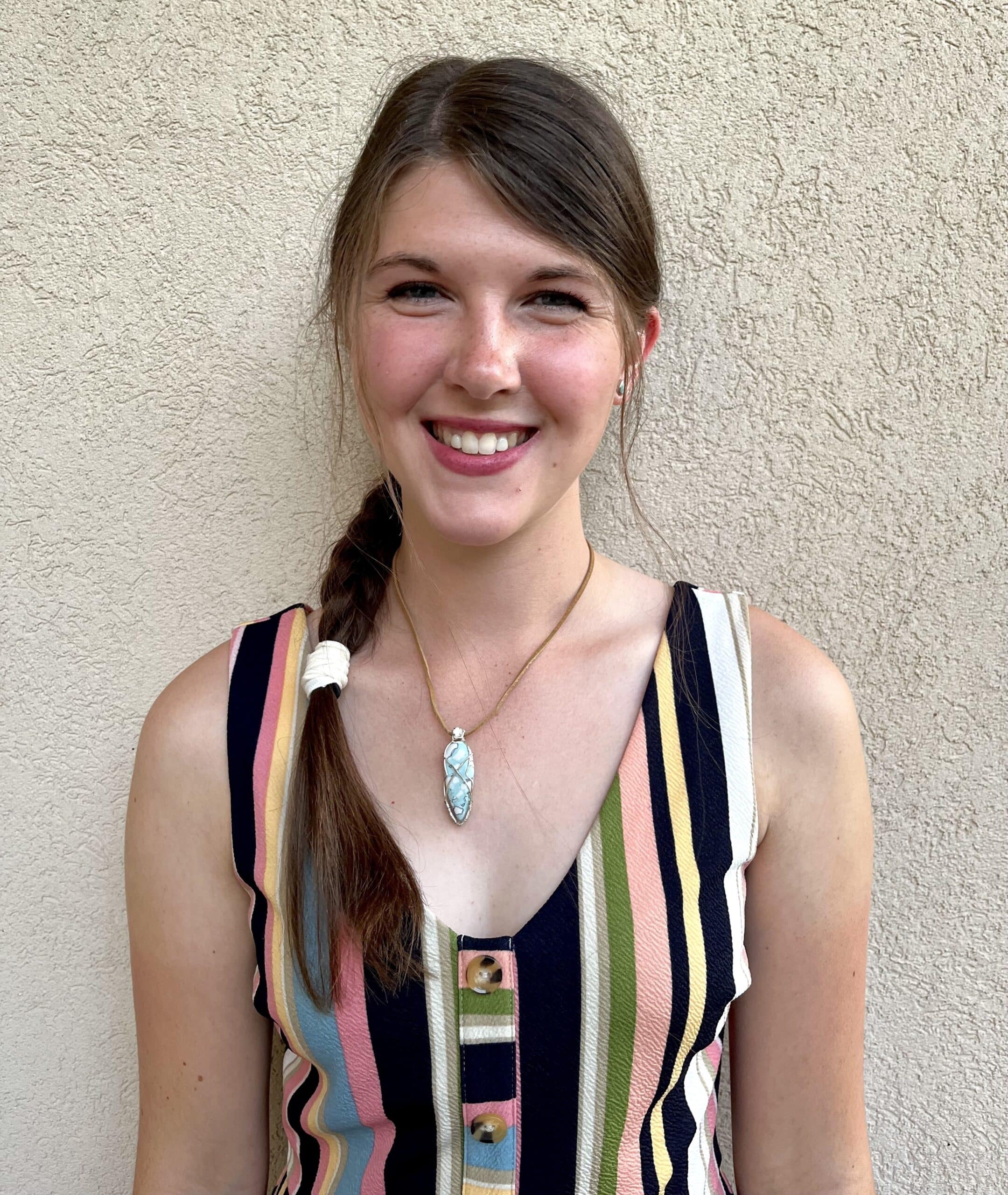 Kathryn Ribbens, a young brown-haired woman wearing a colorful striped dress, poses and smiles at the camera. Photo provided by Kathryn Ribbens.