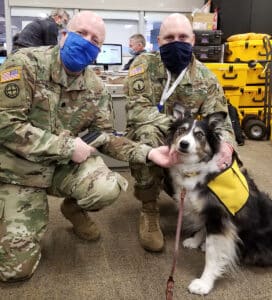 Two active Army servicemen and pictured petting a dog in a Pet Partners vest.