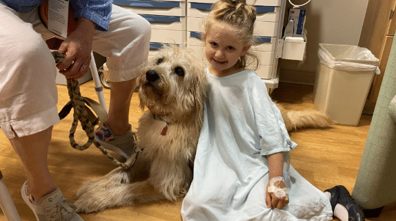 A child in a hospital gown hugging a dog