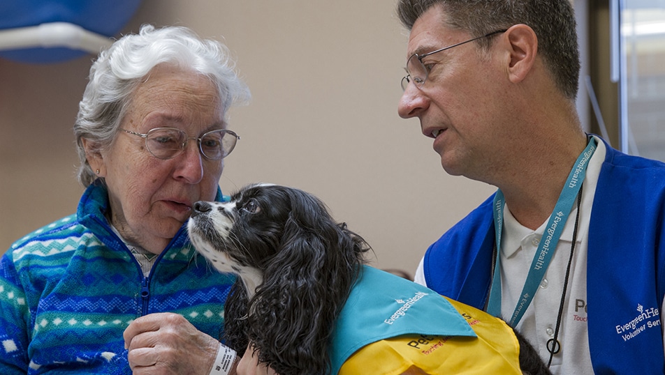 Older woman looks lovingly at Pet Partners therapy dog being held by her handler.