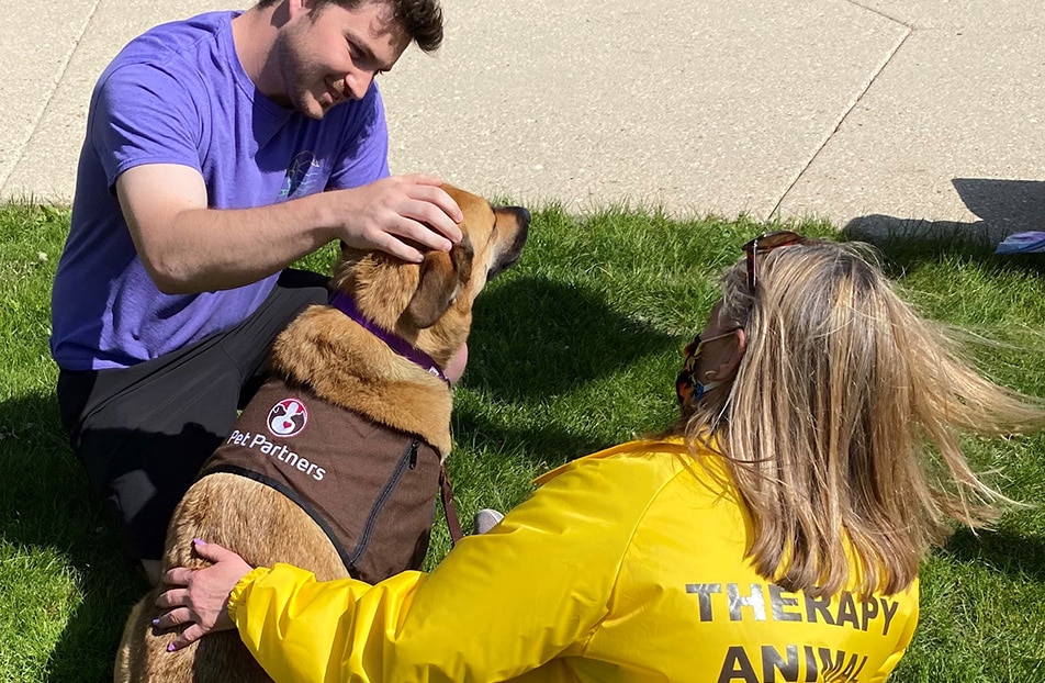 Therapy animal team on a visit with a man petting the dog on the head.