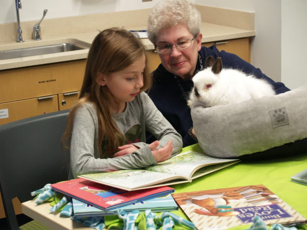 Child reading to a therapy rabbit and a volunteer handler.