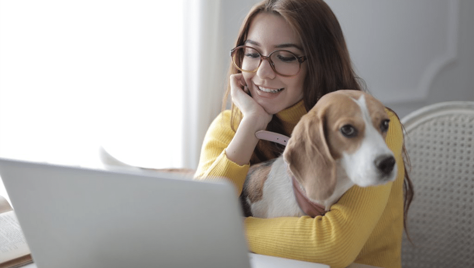 Woman sits in front of laptopn, holding dog on her lap.