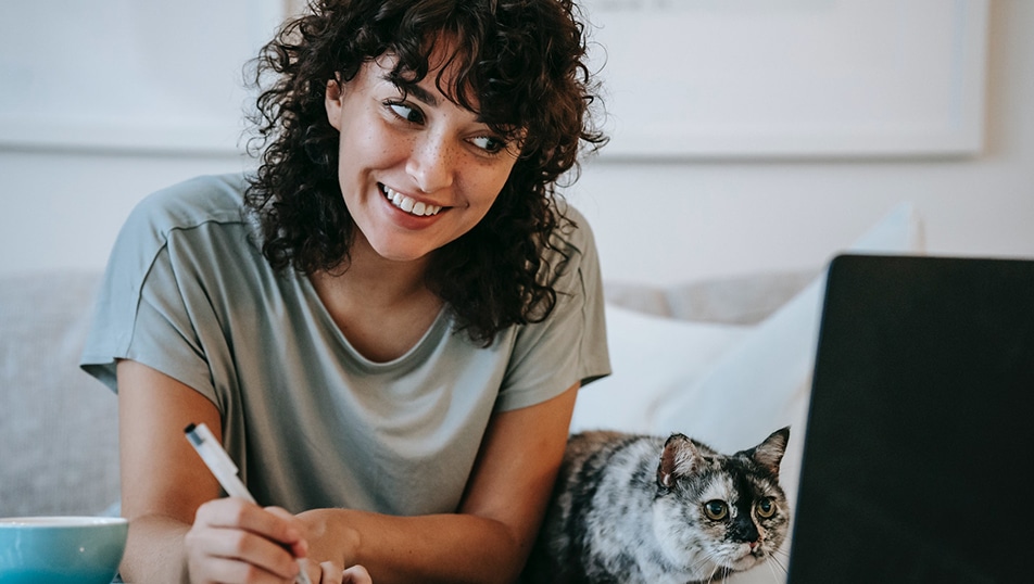 A woman and her cat look at a laptop screen.