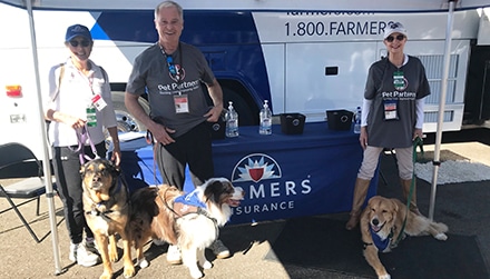 Pet Partners teams pose at a Farmers Insurance booth at an event.