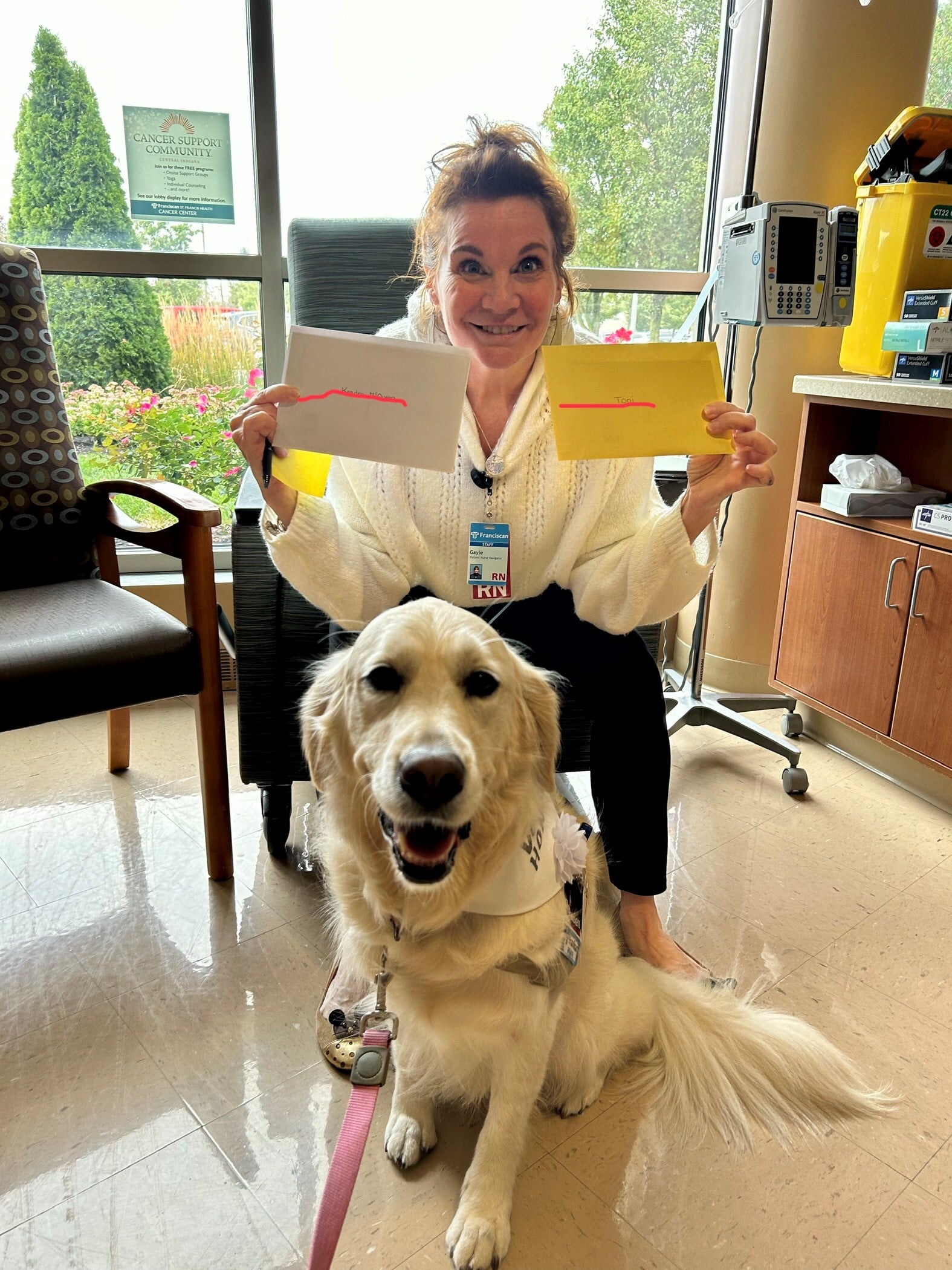 A woman holds up 2 cards, while a therapy dog sits in front of her.